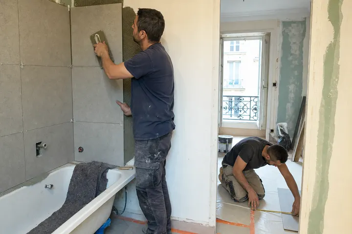 Illustration IA : deux artisans posent du carrelage dans une salle de bain en travaux